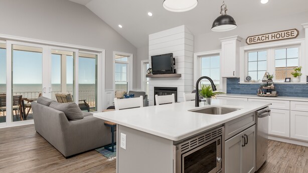 A modern kitchen with a large island, white cabinetry, and a view of the beach.
