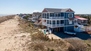 A beachfront property with a large two-story house, a covered patio, and a beach view.