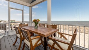 A wooden deck with a table and chairs, overlooking a beach.