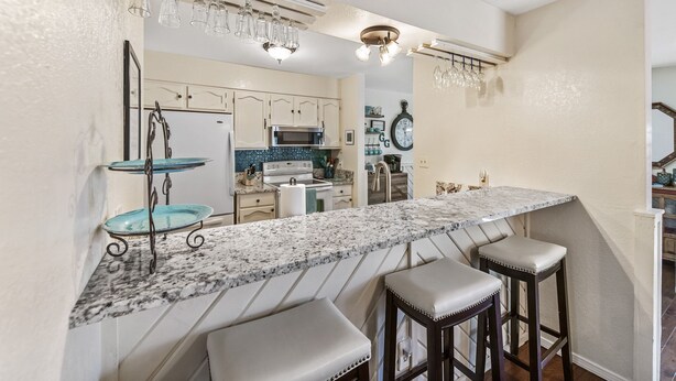 A kitchen with a marble countertop, two bar stools, and hanging light fixtures. - Gertie’s Getaway Mountain Retreat Family Friendly  Couples Weekend (Ruidoso)