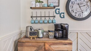 A wall-mounted clock, a coffee machine, and a mug rack with teal mugs. - Gertie’s Getaway Mountain Retreat Family Friendly  Couples Weekend (Ruidoso)