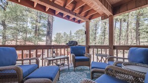 A covered outdoor seating area with wicker furniture and blue cushions, overlooking a forested area. - Gertie’s Getaway Mountain Retreat Family Friendly  Couples Weekend (Ruidoso)
