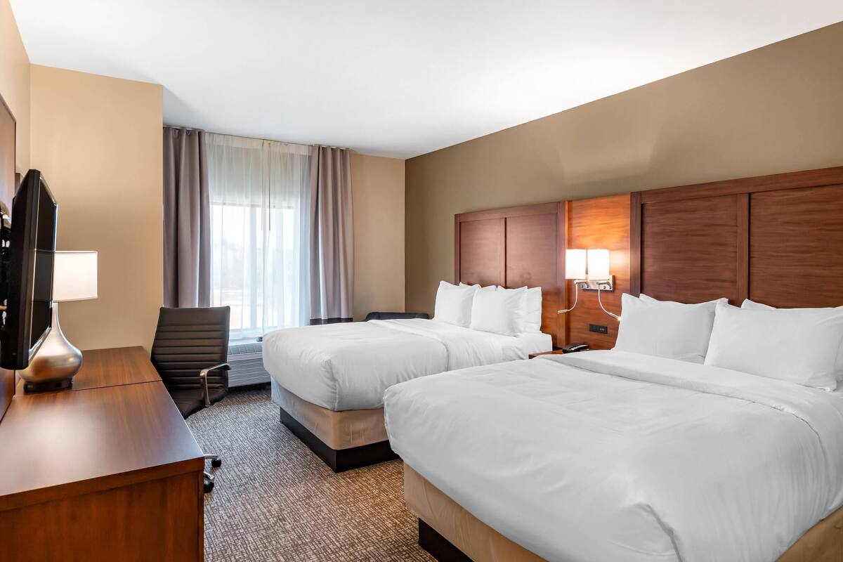 A hotel room with two beds, a desk, a chair, a TV, and a window with curtains.