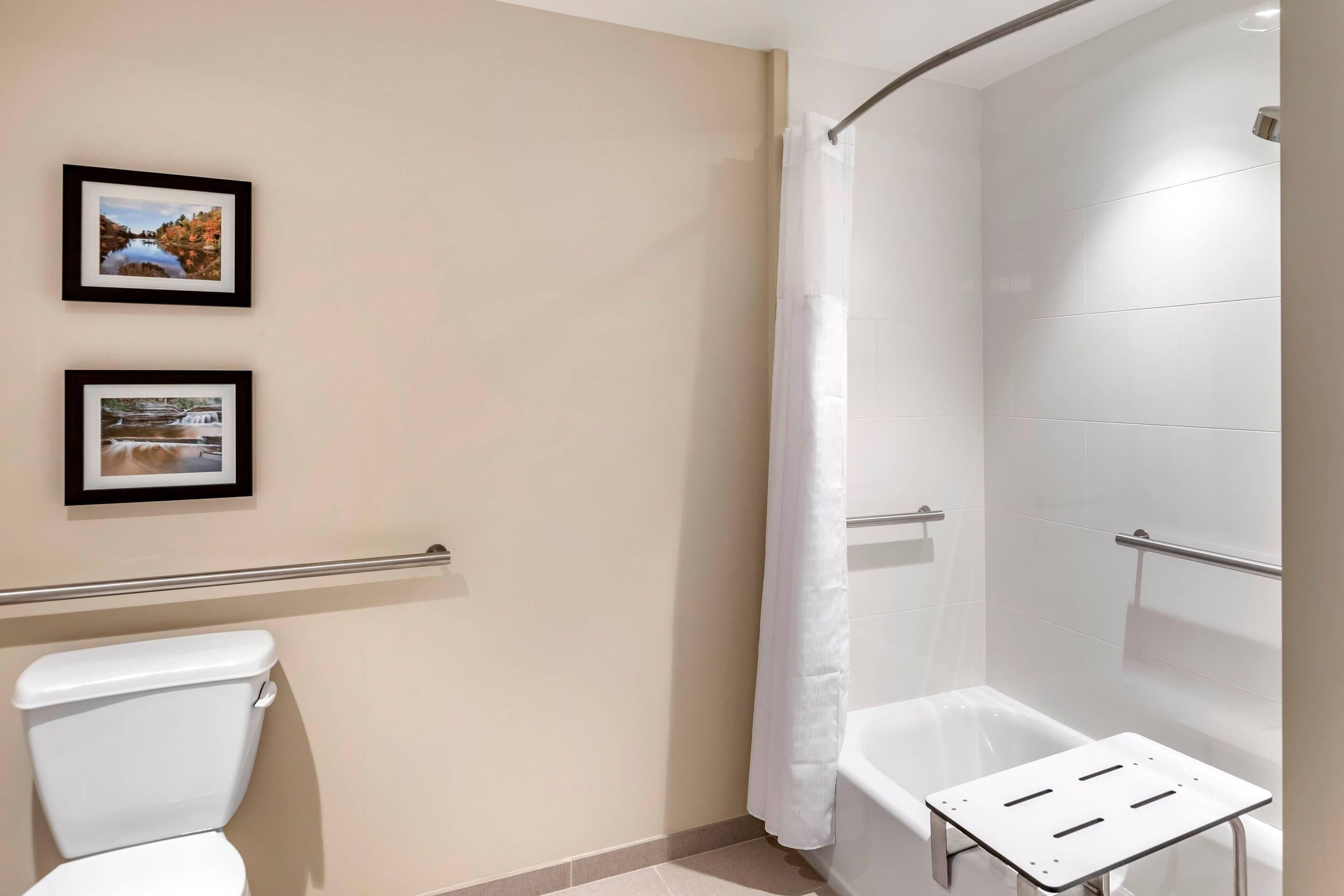 Ein Badezimmer mit Toilette, einer Dusche mit weißem Vorhang und zwei gerahmten Bildern an der Wand.