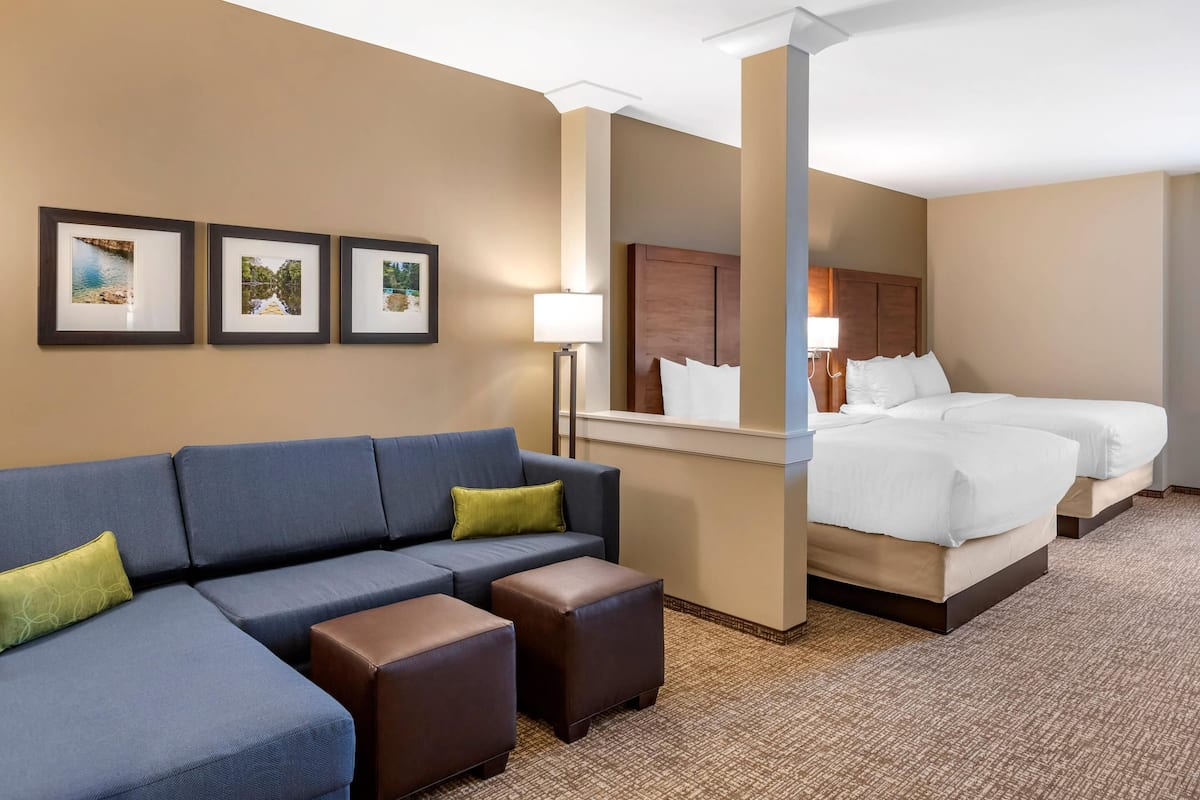A hotel room with a blue sofa, two ottomans, a bed with white linens, and three framed pictures on the wall.