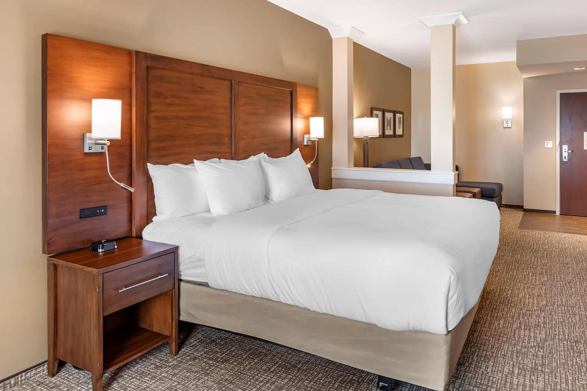 A hotel room with a large bed, wooden headboard, bedside lamps, a nightstand, and a mirror.