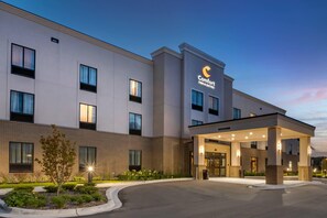 A Comfort Inn & Suites building with a well-lit entrance, a landscaped garden area, and a clear sky.