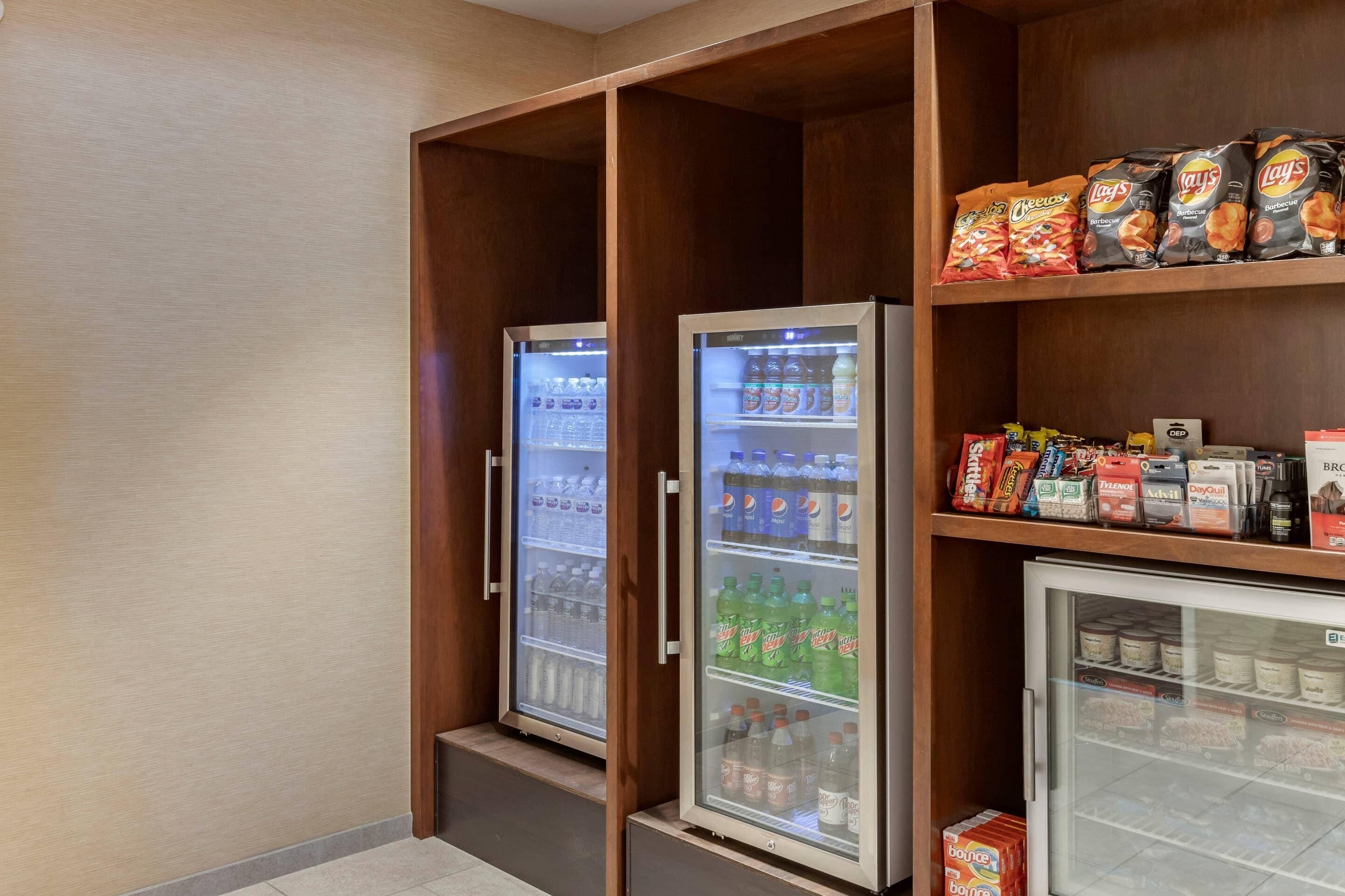 A hotel room with a minibar, a refrigerator stocked with beverages, and snacks on shelves.