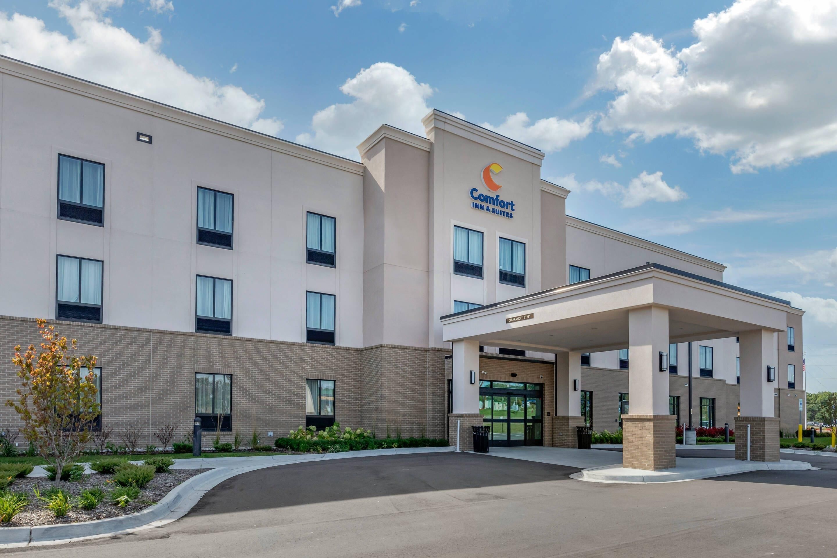 A Comfort Inn & Suites building with a covered entrance, multiple windows, and a landscaped area with plants.