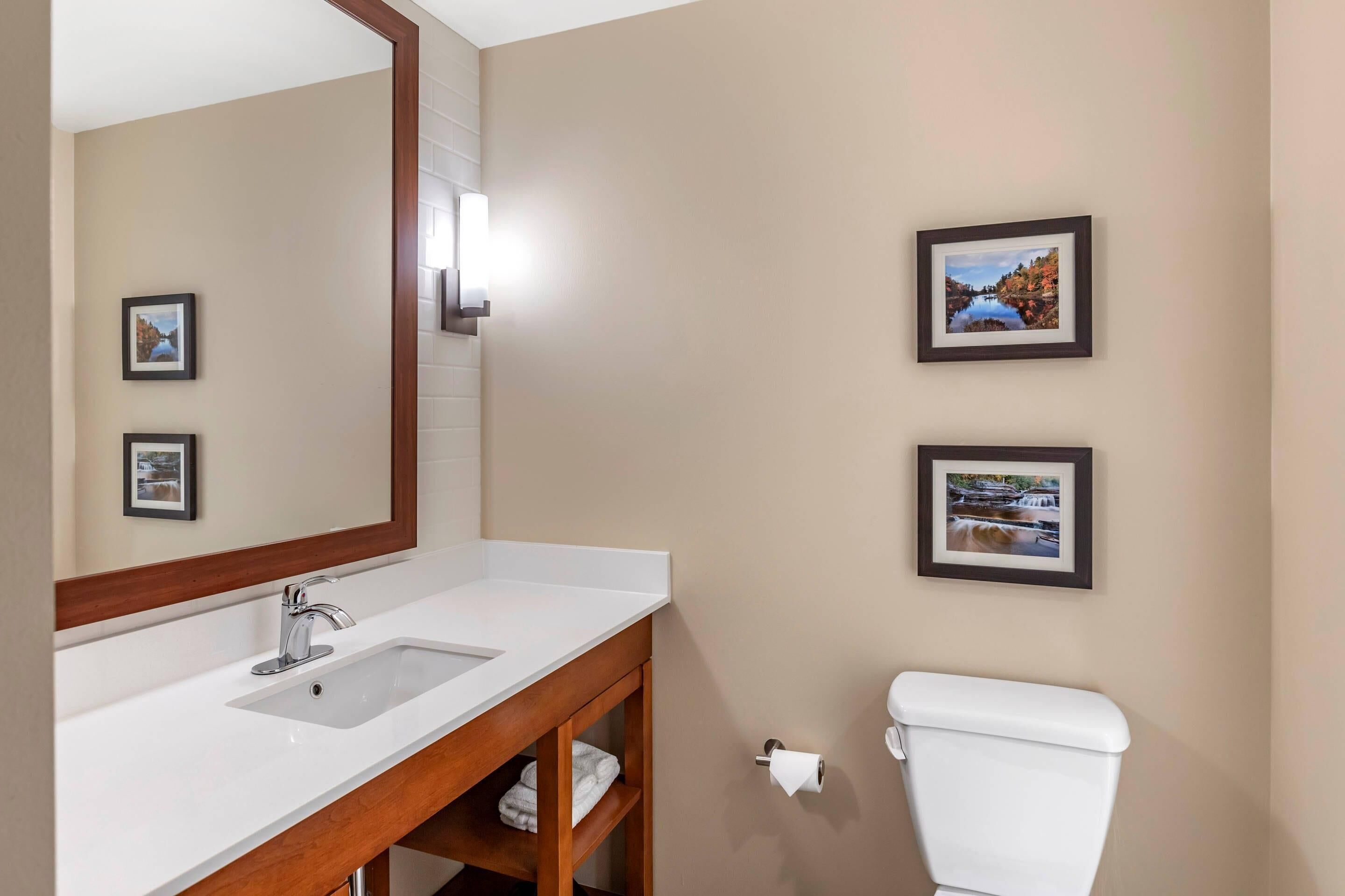 A bathroom with a white sink, a mirror, a toilet, and three framed pictures on the wall.