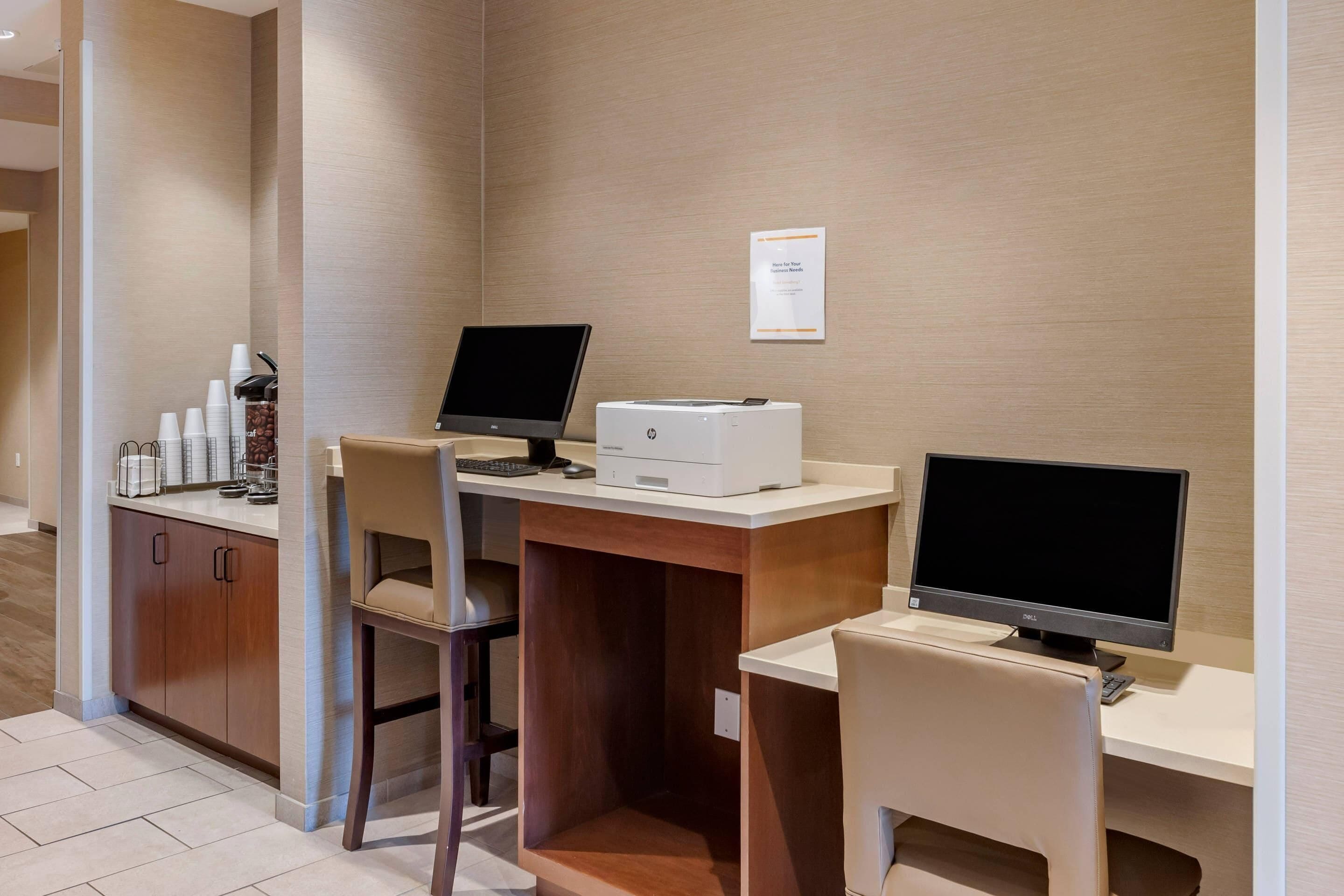 Habitación de hotel con escritorio, dos monitores, impresora y estación de café.