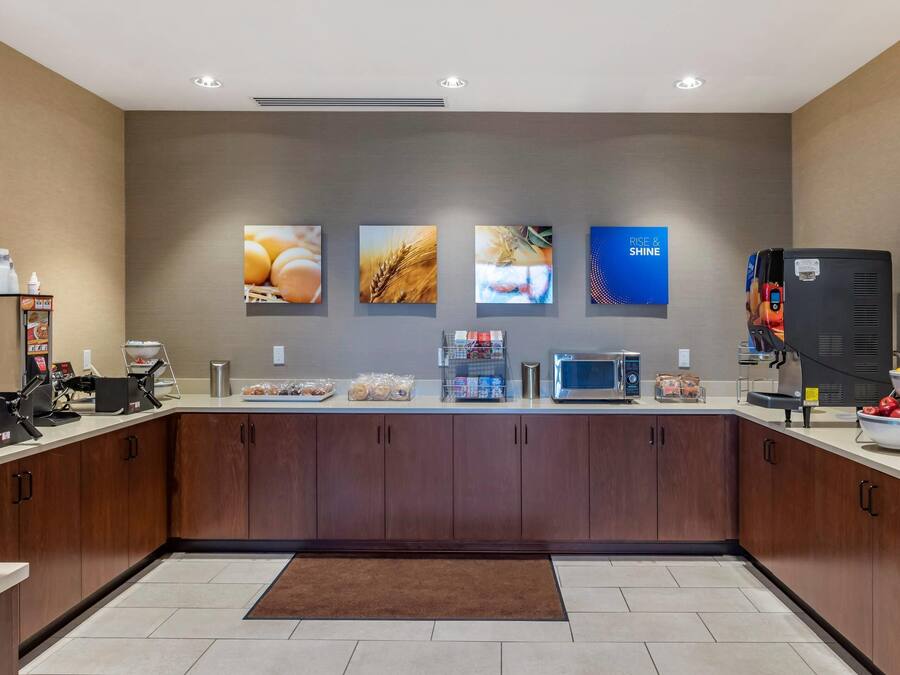 A modern kitchen with a microwave, coffee maker, and a refrigerator. There are food items on the counter and a coffee station.