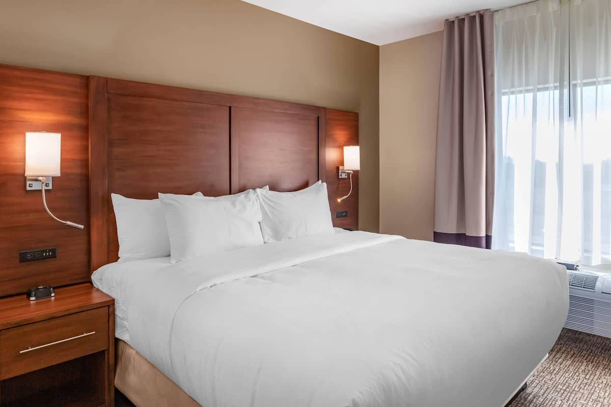 A hotel room with a large bed, wooden headboard, bedside lamps, a nightstand, and a window with curtains.