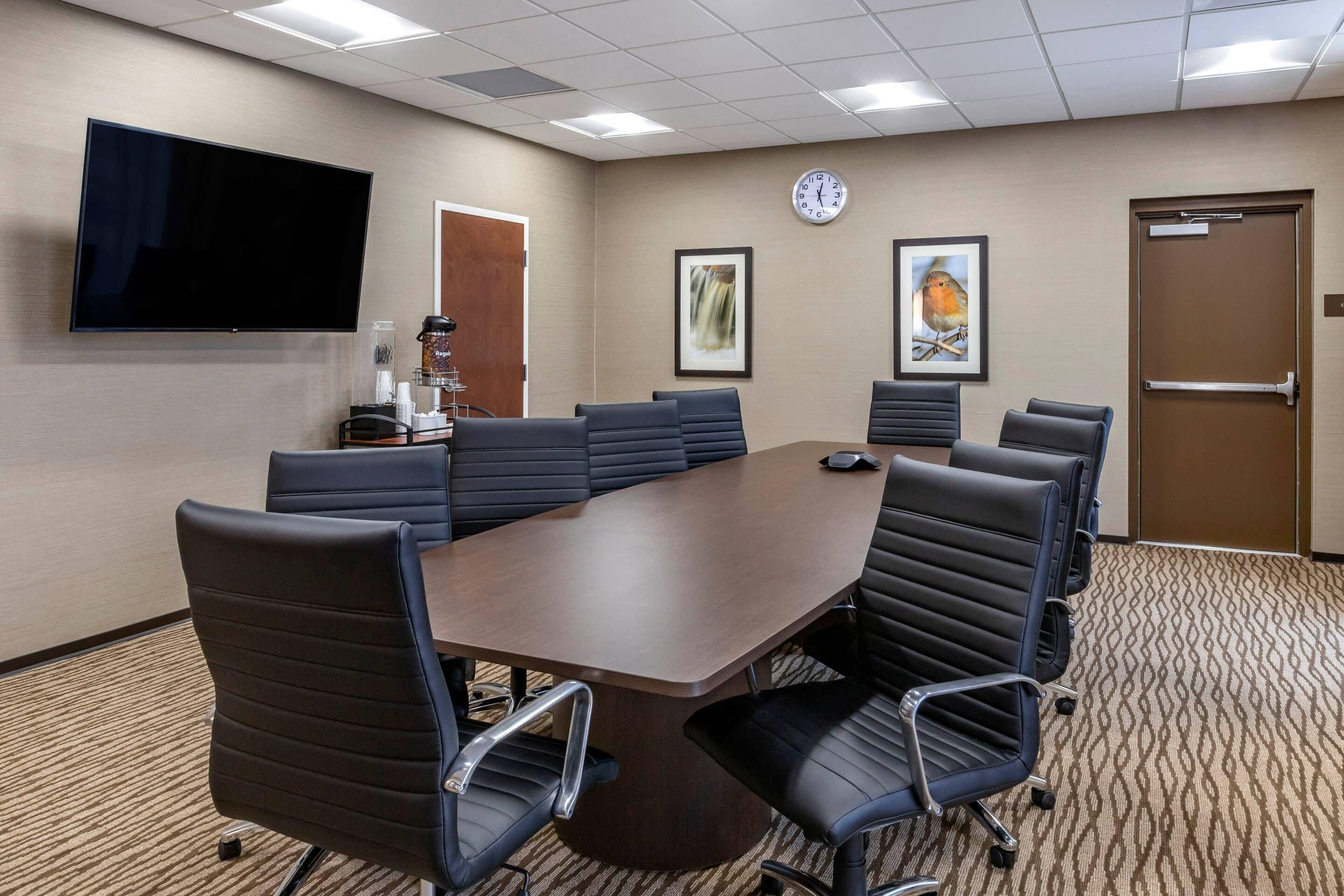 A conference room with a large table, multiple chairs, a clock, framed artwork, and a television.
