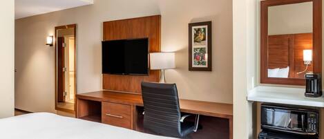 A hotel room with a bed, a desk with a flat-screen TV, a chair, a lamp, a coffee maker, and a microwave.