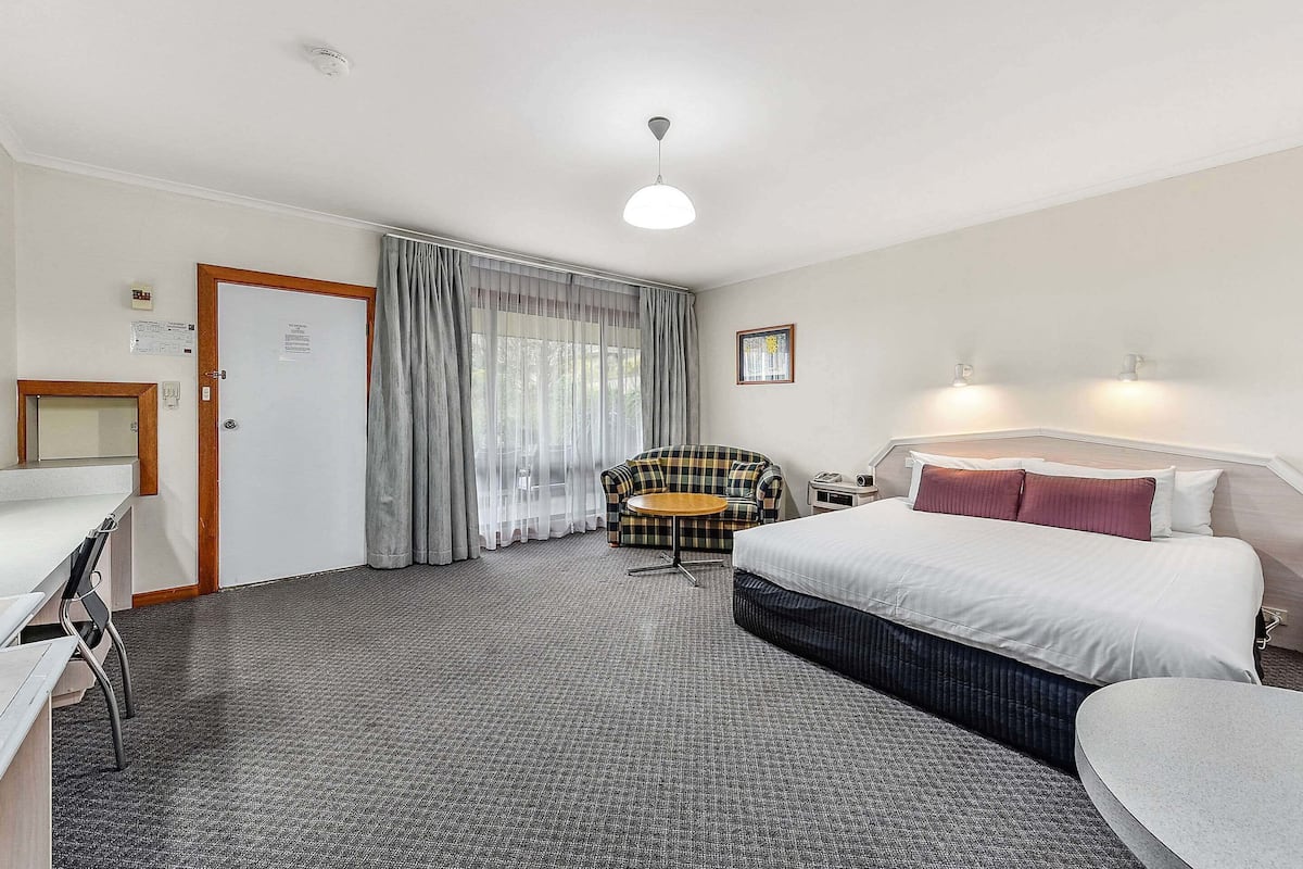 Ein Hotelzimmer mit Bett, Schreibtisch, Stuhl, kleinen Tisch und einem Fenster mit Vorhängen.