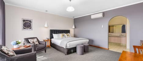 Una habitación de hotel con una cama, una silla, una mesita con un florero y un espejo en la esquina.