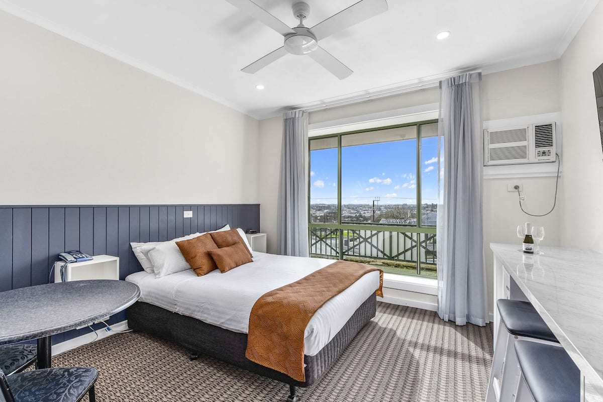 Ein Hotelzimmer mit Bett, Schreibtisch, Stuhl, einem Balkon mit Blick und einer Klimaanlage.