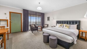 A hotel room with a large bed, two armchairs, a small table, and a view of the city through the window. - Comfort Inn The Lakes (Mount Gambier)