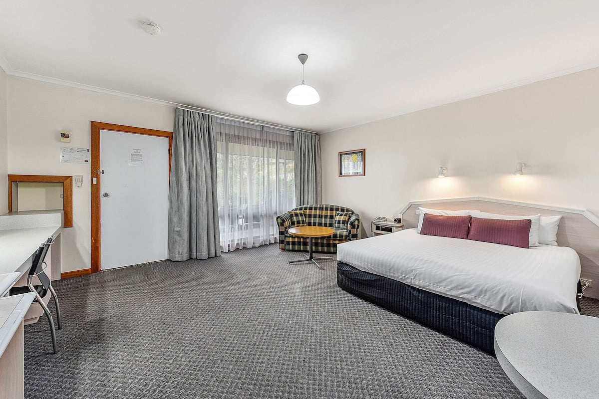Ein Hotelzimmer mit Bett, Schreibtisch, Stuhl, rundem Tisch und einem Fenster mit Vorhängen.