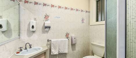 A bathroom with a sink, mirror, toilet, and hand soap dispenser.
