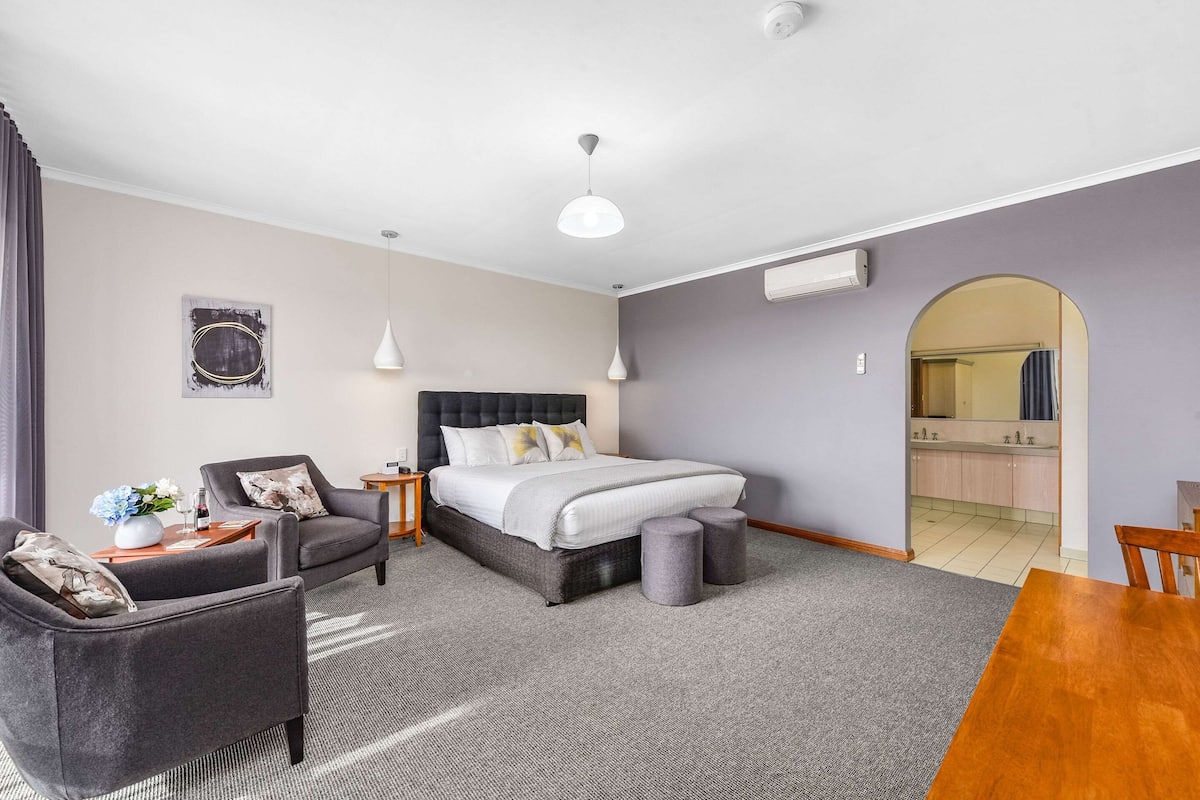 Ein modernes Hotelzimmer mit einem Bett, zwei Sesseln, einem kleinen Tisch und einem Esstisch.