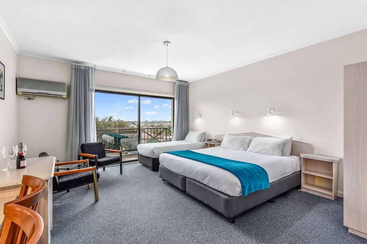 Ein Hotelzimmer mit zwei Betten, einem Essbereich inklusive Tisch und Stühlen, einem an der Wand befestigten Fernseher und einem Balkon mit Blick.