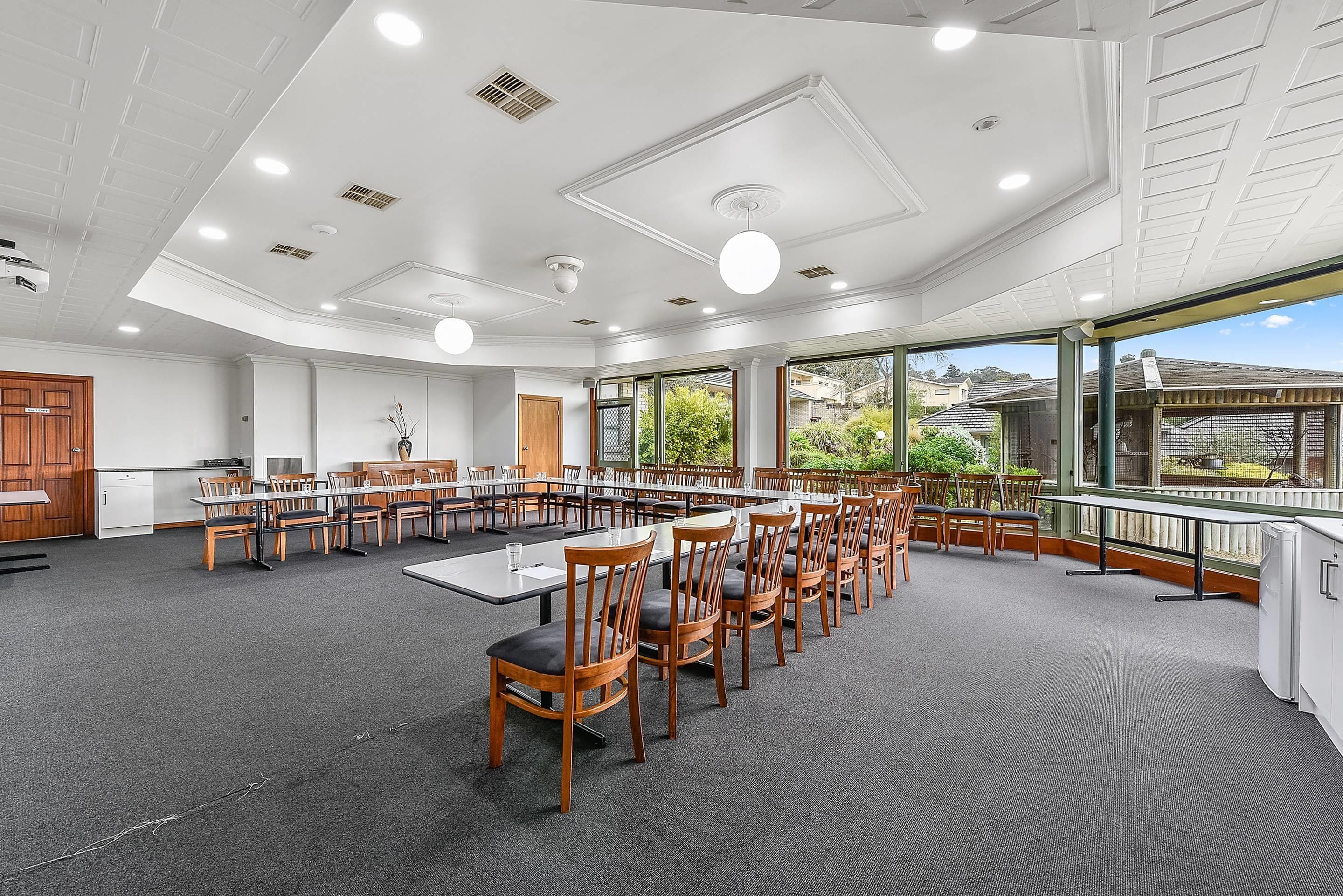 Un salón de conferencias con varias mesas y sillas, ventanas amplias y vistas al exterior.