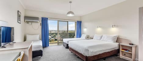 Habitación de hotel con dos camas, un escritorio, un televisor y un balcón con cortinas azules.