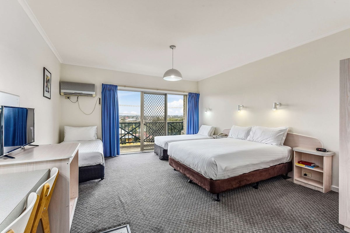 Ein Hotelzimmer mit zwei Betten, einem Schreibtisch, einem Fernseher, einem Kleiderschrank und einem Balkon mit Blick.