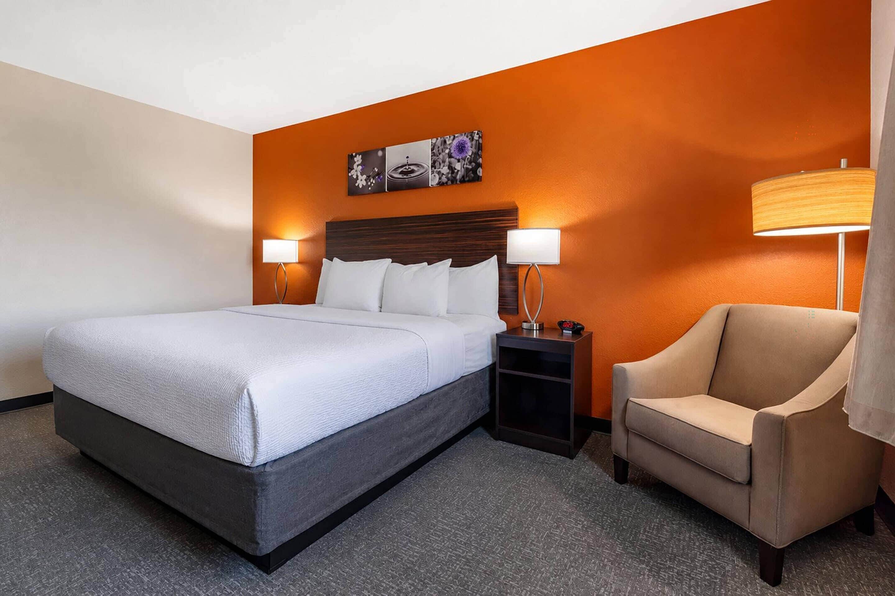Habitación de hotel con cama, mesita de noche, silla y una pared con un cuadro.