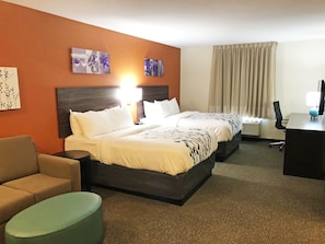 Een hotelkamer met een tweepersoonsbed, een bureau met een computer, een stoel, een bank en een klein voetenbankje.