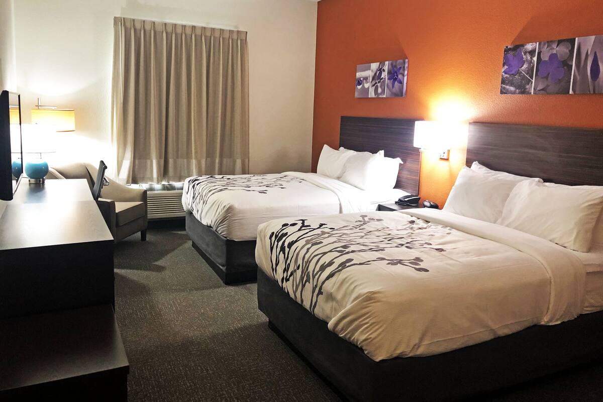 A hotel room with two beds, a desk, a chair, a lamp, and a window with curtains.