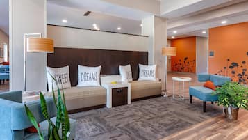 A modern hotel lobby with a sofa bed, a blue armchair, a small table, and a potted plant.