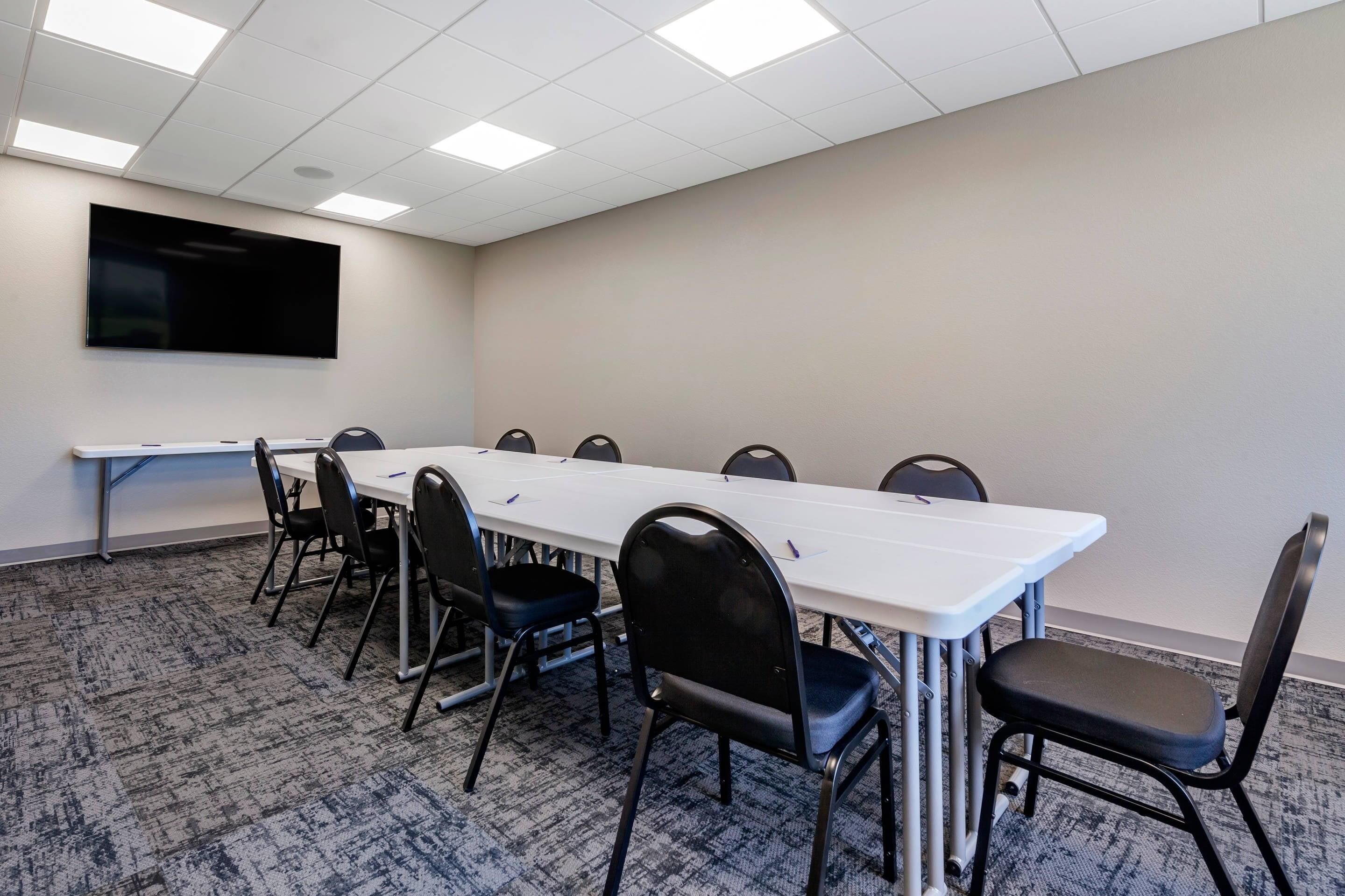 A conference room with a long table, chairs, a flat-screen TV, and carpeted flooring.