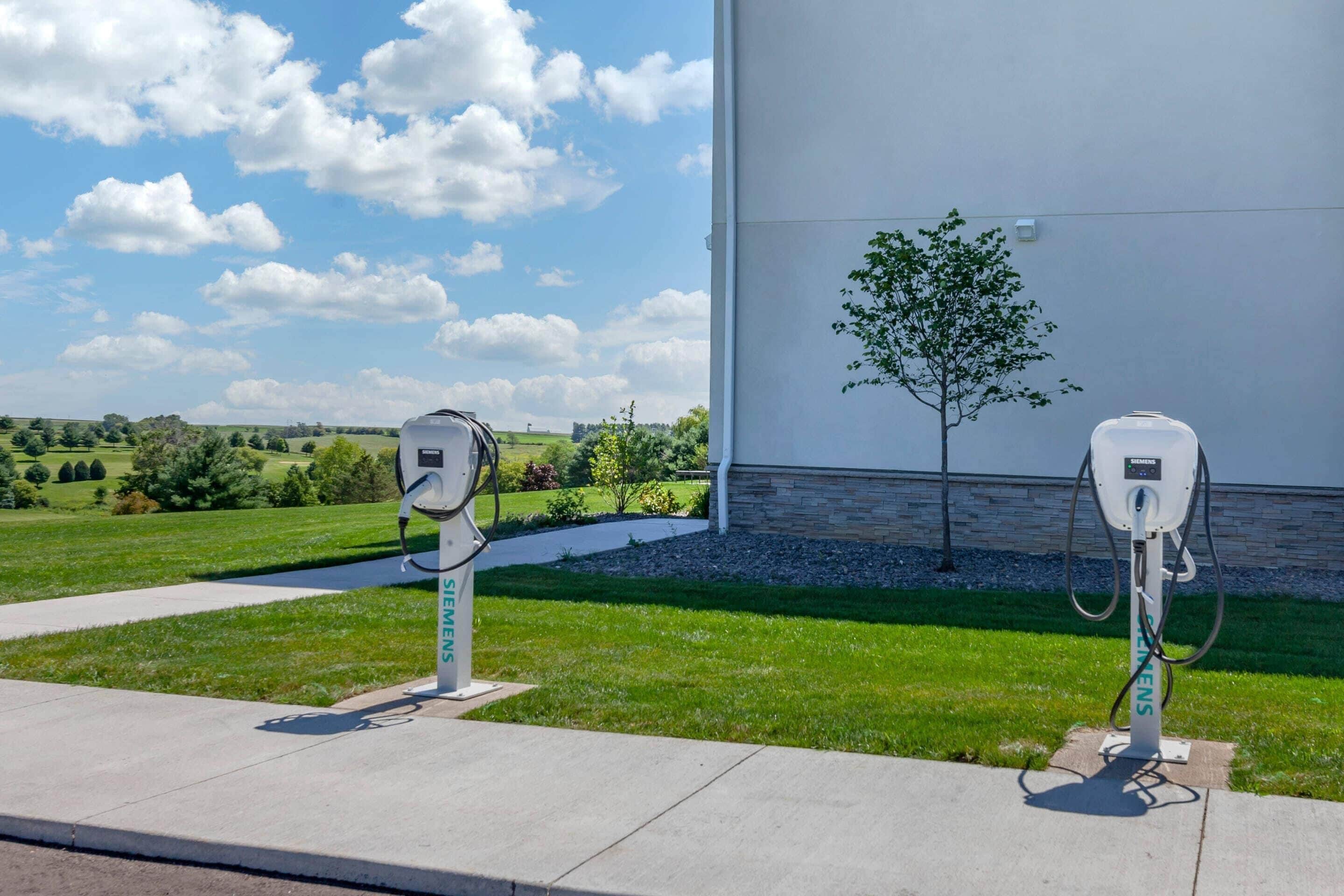 Two electric vehicle charging stations in front of a building with a landscaped garden and a clear sky.