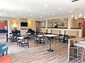 Een modern restaurant met houten vloeren, verschillende zithoeken met zowel zitbanken als tafels, en een bar met krukken.