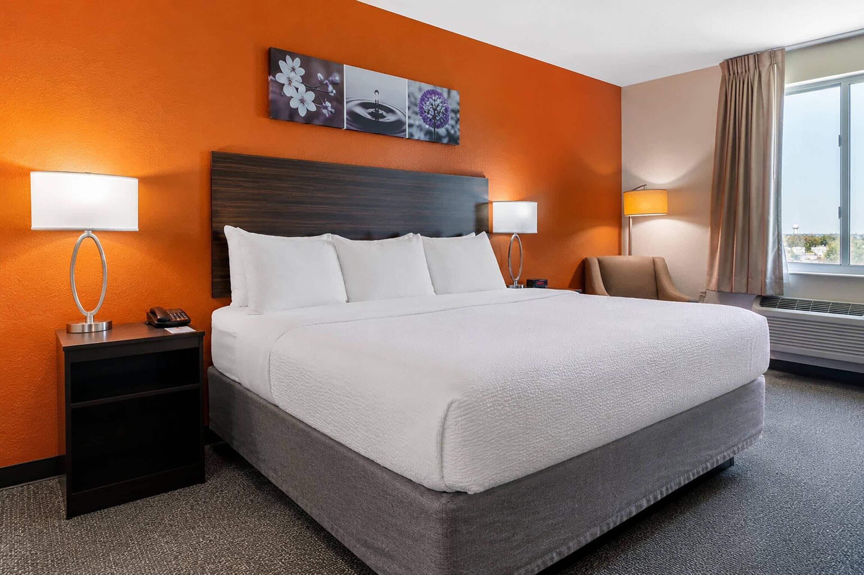 Une chambre d’hôtel avec un grand lit, deux tables de chevet avec des lampes, une chaise et une fenêtre avec des rideaux.