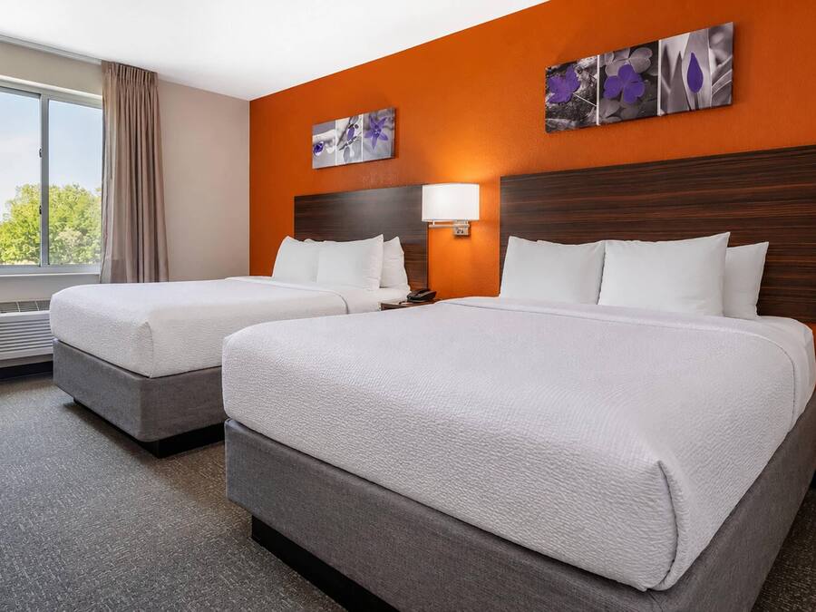 Una camera d'albergo con due letti, una finestra con tende, una lampada a parete e un quadro.