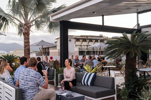 An outdoor seating area with a mix of seating arrangements, including a sofa and chairs, under a covered section with umbrellas. - The Benson Hotel (Cairns)