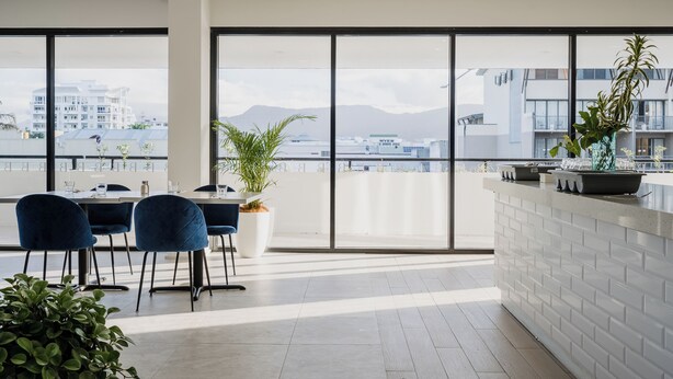A modern dining area with large windows, a white brick counter, and blue chairs. - The Benson Hotel (Cairns)
