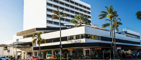 A modern hotel with a white facade, multiple floors, and a ground-level retail area.
