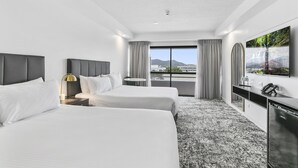 A hotel room with two beds, a desk, a TV, and a view of the city. - The Benson Hotel (Cairns)