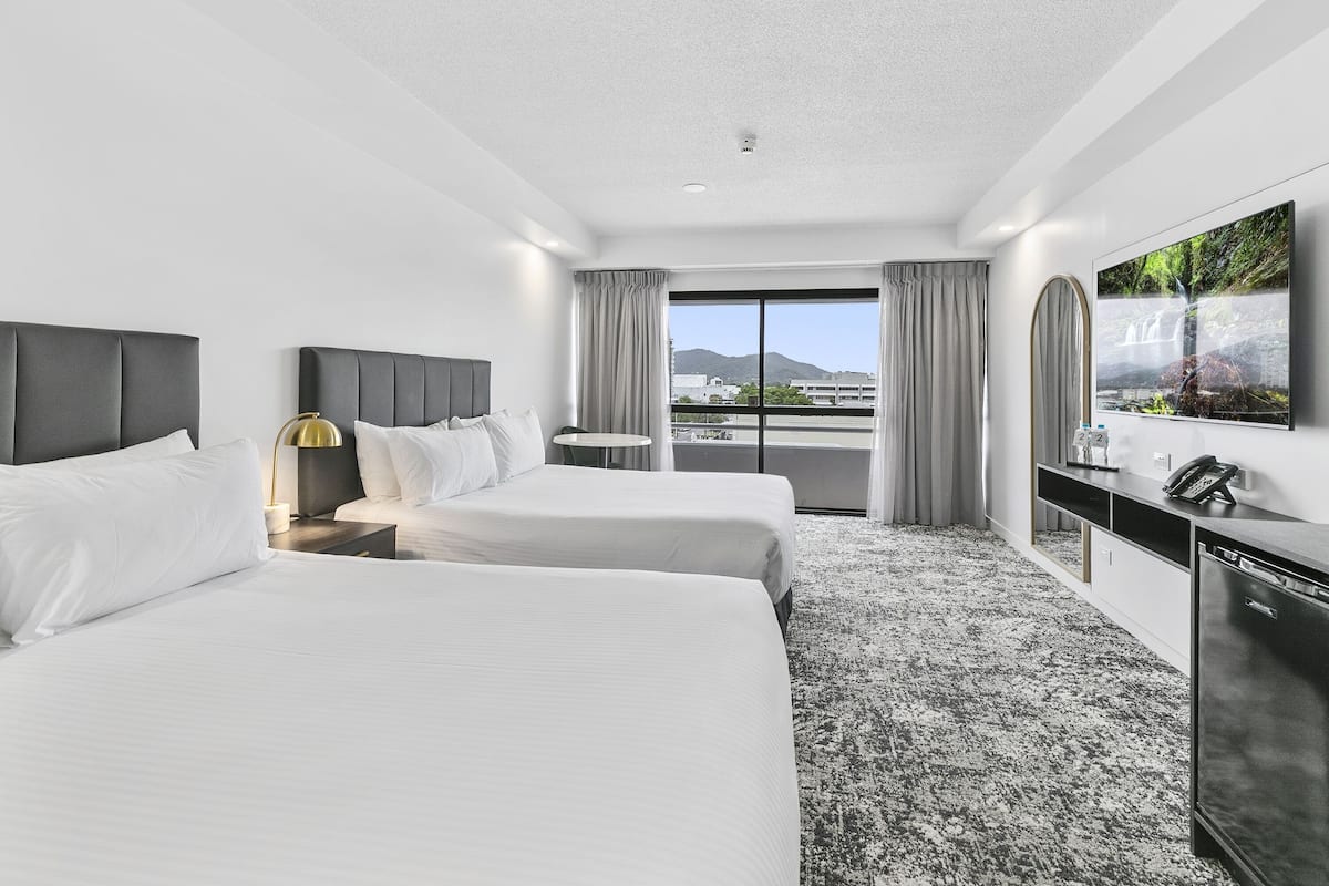 A hotel room with two beds, a desk, a TV, and a view of the city.