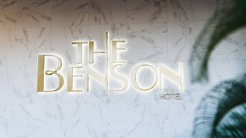 A hotel sign with the name "The Benson Hotel" in illuminated letters against a marble wall.