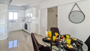 A modern kitchen with white cabinets, a dining area with a glass table, and a round mirror on the wall. - Phaedrus Living: Seaside Luxury Flat Lighthouse 65 (Paphos)