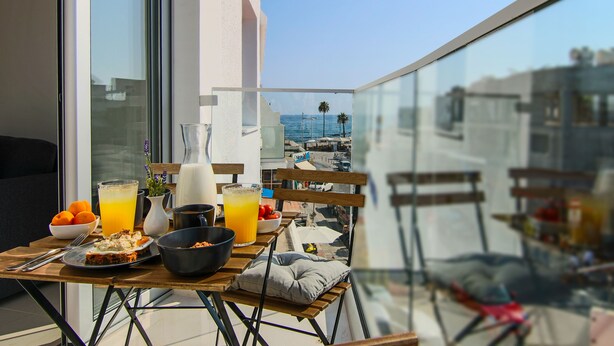 A balcony with a table set for breakfast, including orange juice, a bowl of fruit, and a plate of food. - Phaedrus Living: Seaside Luxury Flat Lighthouse 65 (Paphos)