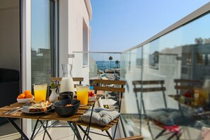 A balcony with a table set for breakfast, including orange juice, a bowl of fruit, and a plate of food. - Phaedrus Living: Seaside Luxury Flat Lighthouse 65 (Paphos)