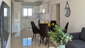A modern living room with a grey sofa, a dining table with chairs, and a potted plant. - Phaedrus Living: Seaside Luxury Flat Lighthouse 65 (Paphos)