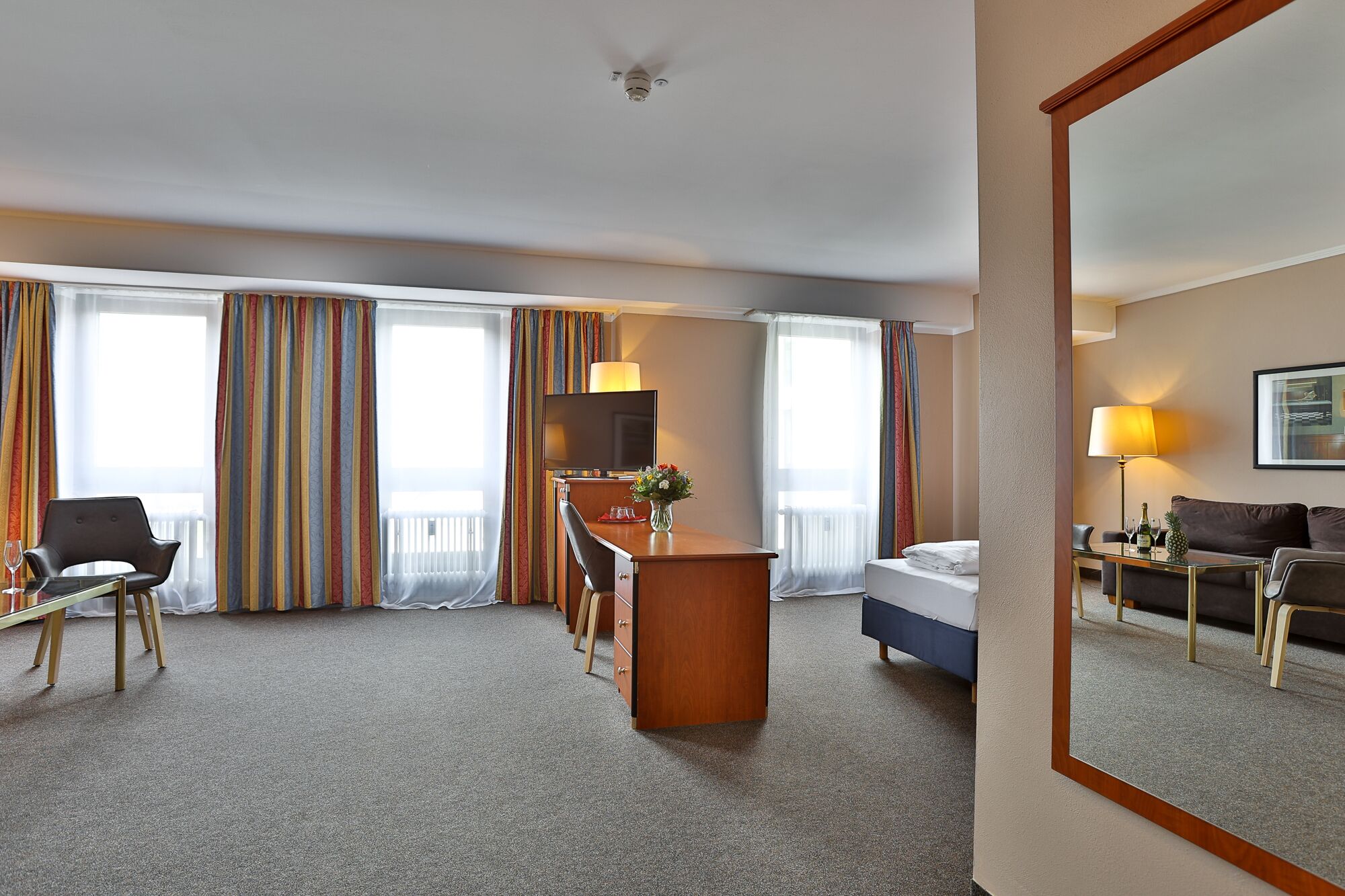 Ein Hotelzimmer mit Bett, Schreibtisch mit Stuhl, Sofa, Couchtisch und Fernseher.